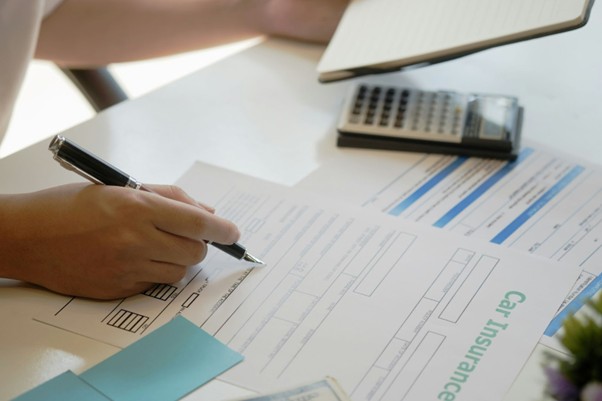  A hand of a person filling in a car insurance policy, highlighting key factors such as the policy type for choosing the best time to renew car insurance.